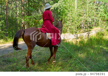 Woman in red dress rides a horse in early spring Woman in red dress rides a horse in early spring 94798391