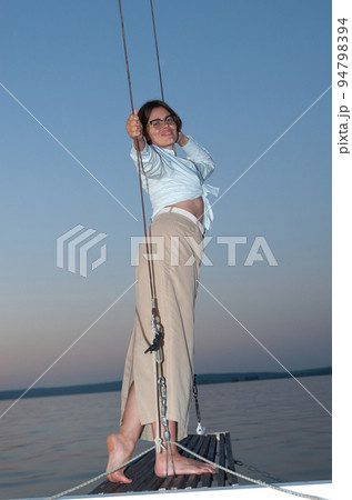 Beautiful woman in casual clothing standing on the bow of a sailing yacht 94798394