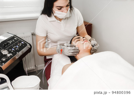 Microcurrent therapy. Cosmelotologist makes stimulating facial massage with electric gloves. Lymphatic drainage massage 94800396