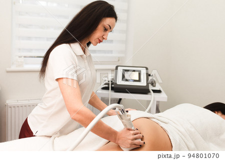 Doctor cosmetologist with a roller in his hands makes a buttocks massage with device.. Doctor cosmetologist with a roller in his hands makes a buttocks massage with device.. 94801070