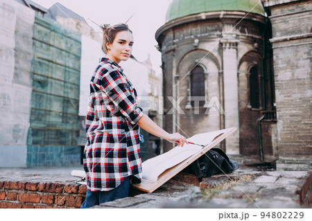 Woman is painting directly on the city street against the background of old architecture. Young painter artist in work. Woman is painting directly on the city street against the background of old architecture. Young painter artist in work. 94802229