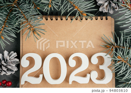 Happy New Year 2023. White numbers 2023 lying on folded notebook with Christmas tree branches and pine cones, copy space Happy New Year 2023. White numbers 2023 lying on folded notebook with Christmas tree branches and pine cones, copy space 94803610
