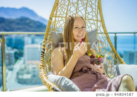 Portrait of gorgeous woman wearing beautiful dress sitting in a patio and eating strawberry 94804587