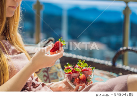Portrait of gorgeous woman wearing beautiful dress sitting in a patio and eating strawberry 94804589