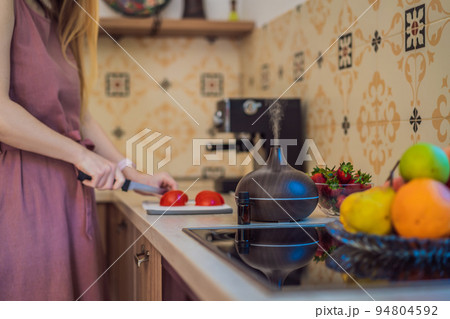 Woman prepares food next to an aroma diffuser. cook cuts ripe red peppers in the kitchen. Cooking fresh, ripe, bell pepper salad for guests. Summer fresh vegetable salad Woman prepares food next to an aroma diffuser. cook cuts ripe red peppers in the kitchen. Cooking fresh, ripe, bell pepper salad for guests. Summer fresh vegetable salad 94804592