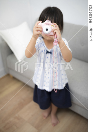 自宅の部屋でおもちゃのカメラを撮って遊ぶ女の子 94804732