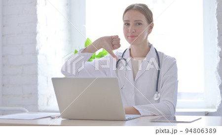 Lady Doctor Showing Thumbs Down While sitting in Clinic Lady Doctor Showing Thumbs Down While sitting in Clinic 94806389
