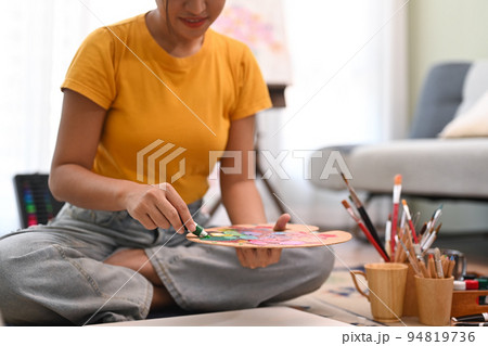 Cropped view of young creative woman holding painting brush and mixing color oil painting on palette Cropped view of young creative woman holding painting brush and mixing color oil painting on palette 94819736