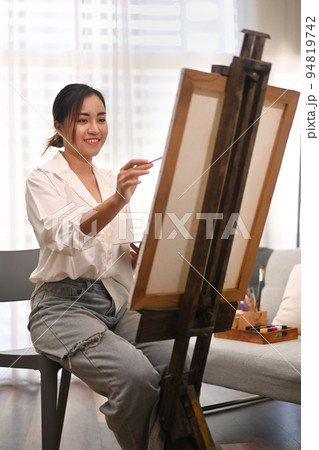 Pleasant millennial woman painting picture on canvas with oil paints in home studio. Leisure activity, creative hobby and art concept 94819742