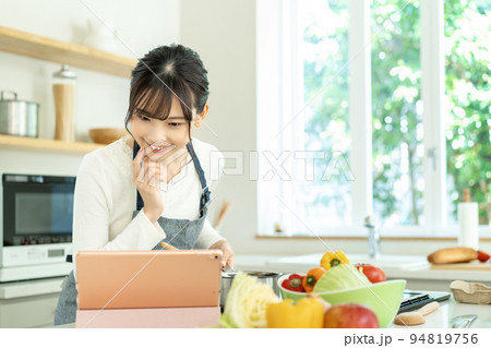 レシピを見ながら料理をするエプロンをした若い女性 レシピを見ながら料理をするエプロンをした若い女性 94819756