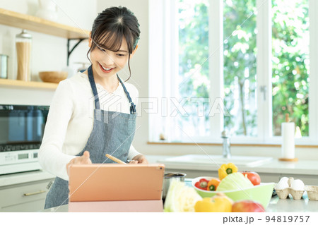 レシピを見ながら料理をするエプロンをした若い女性 94819757