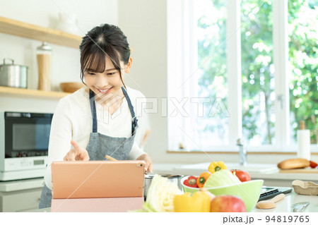 レシピを見ながら料理をするエプロンをした若い女性 94819765