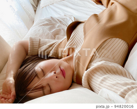 目を閉じてベッドに横たわる女性の写真 94820016