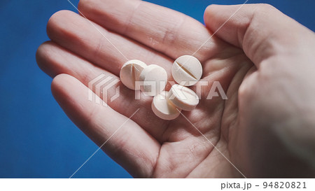 Man takes medicine. Round white pills in male hands. 94820821