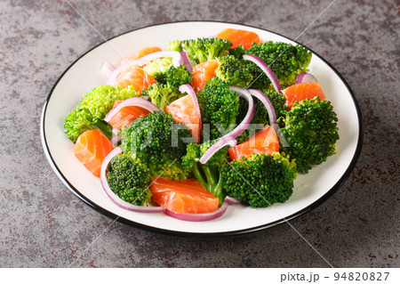 Vitamin salad of steamed broccoli, salted salmon and fresh red onion seasoned with olive oil close-up in a plate. horizontal 94820827