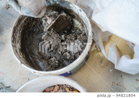 a gloved man's hand kneads cement mortar with a trowel. a gloved man's hand kneads cement mortar with a trowel. 94821804