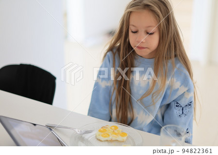 little girl has breakfast at home in the kitchen watching her tablet. Happy child eats eggs and cheese mozzarella little girl has breakfast at home in the kitchen watching her tablet. Happy child eats eggs and cheese mozzarella 94822361