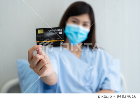 Happy Asian woman wearing a medical mask and holding mock up credit card /insurance card and ok sign in a hospital bed. Insurance policy by bank, payment medical treatment concept 94824616
