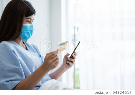 Happy Asian woman wearing a medical mask and holding mock up credit /insurance card and smartphone in a hospital bed for Check health insurance eligibility. Insurance policy by bank, payment medical Happy Asian woman wearing a medical mask and holding mock up credit /insurance card and smartphone in a hospital bed for Check health insurance eligibility. Insurance policy by bank, payment medical 94824617