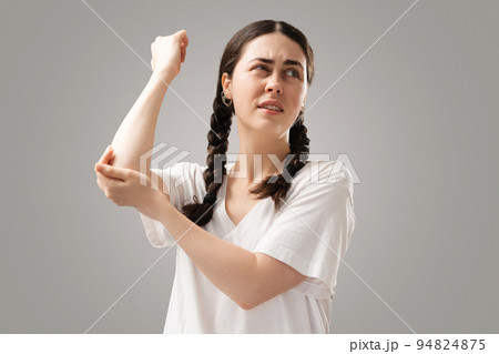 A young woman with dark piggy tails holds her elbow with her hand, feeling pain. Inflammation of the joints. The concept of insurance of health A young woman with dark piggy tails holds her elbow with her hand, feeling pain. Inflammation of the joints. The concept of insurance of health 94824875