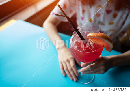 female drinking red grapefruit juicy cocktail with straw in cafe or restaurant 94828582