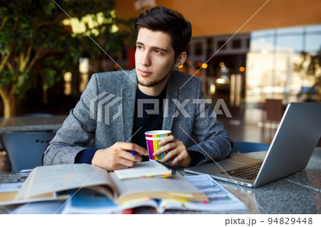 Shot of young male student sitting at table and writing on notebook. Male student studying in cafe. 94829448