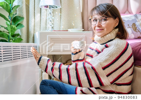 Woman warming herself in bedroom near electric heater Woman warming herself in bedroom near electric heater 94830083