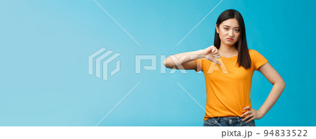 Moody unsatisfied cute asian girl picky, disliking bad restaurant food smirking displeased, grimacing disappointed show thumb down, shaking head negative judgement, stand blue background 94833522