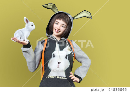 兎の耳のフード付きの衣装を着て片手に兎を乗せている女性 94836846