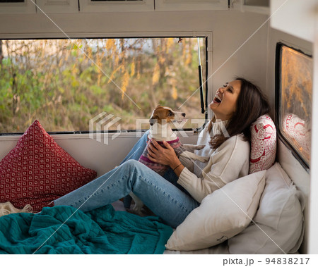 Caucasian woman sitting in a van hugging with dog Jack Russell Terrier. Travel in a camper in the fall. 94838217