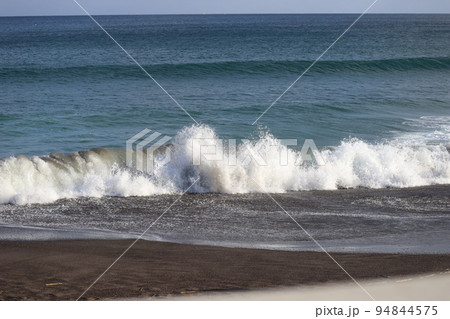 白い波しぶきの巻波の波打ち際と砂浜の海岸と青い海面の海と水平線と ...