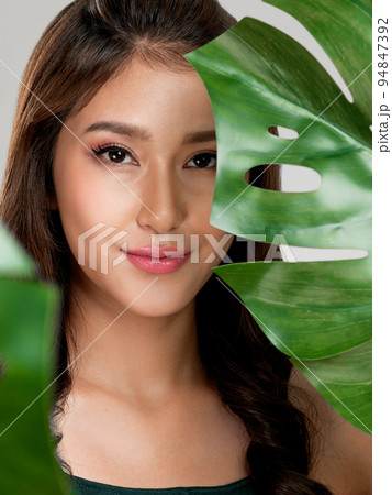 Closeup young ardent woman with healthy skin holding green leaf near her face. 94847392