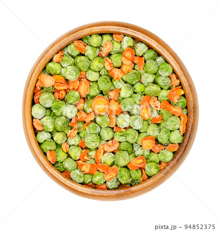 Dehydrated green peas and carrot pieces in a wooden bowl. Mixed vegetables. Seeds of pod fruit Pisum sativum, and cut orange carrots, Daucus carota, a root vegetable. Closeup, from above, food photo. 94852375