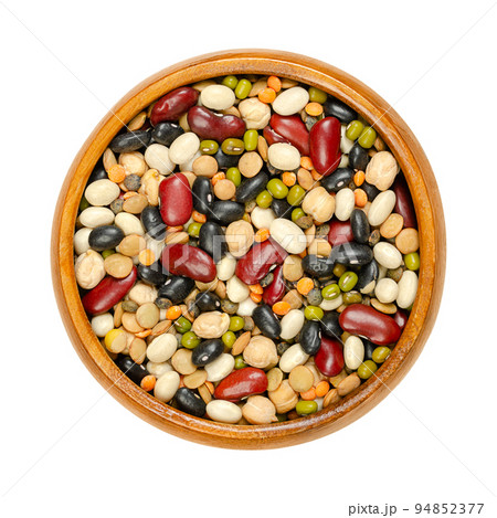 Mixed dried pulses in a wooden bowl, from above. Colorful mix of red kidney, black and white beans, mung beans, brown, green and red lentils, and chickpeas. Isolated, on white background, food photo. 94852377