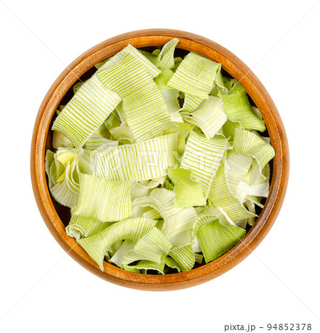Dehydrated leek flakes, from above, in a wooden bowl. Dried strips of Allium porrum, a slightly green, crunchy and firm vegetable, with aromatic, mild and onion-like taste. Isolated, macro food photo. 94852378