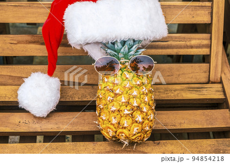 Portrait of relaxing funny pineapplewearing sunglasses and Santa Claus hat lies on wooden sun lounger in sunny weather in tropics. Christmas in tropics. Winter holidays in summer 94854218