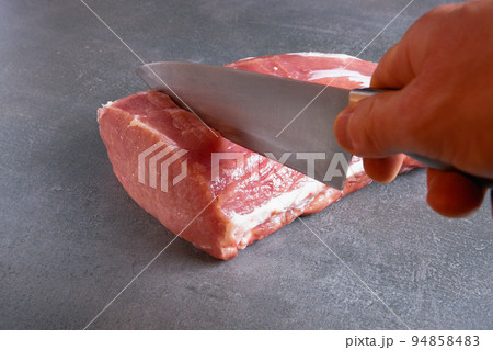 The chef is cutting fresh raw meat into steaks. Close-up on a gray background. The chef is cutting fresh raw meat into steaks. Close-up on a gray background. 94858483