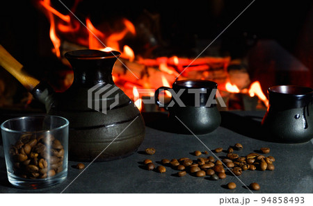 Cezve and coffee cups with coffee beans on the background of a burning fire. Turkish coffee. Cezve and coffee cups with coffee beans on the background of a burning fire. Turkish coffee. 94858493