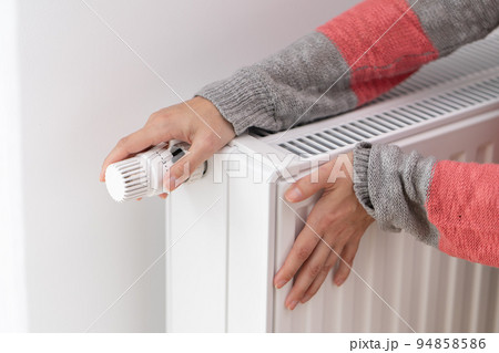 A woman touches a cold radiator of a home heater and increases the heating power A woman touches a cold radiator of a home heater and increases the heating power 94858586