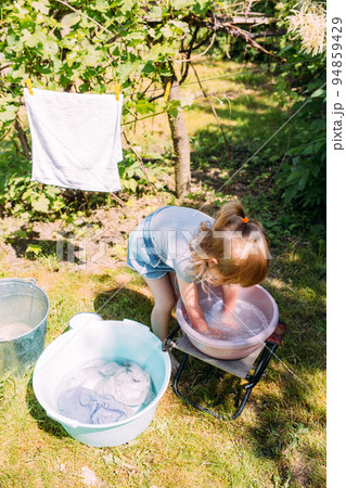 Little preschool girl helps with laundry. Child washes clothes in garden Little preschool girl helps with laundry. Child washes clothes in garden 94859429