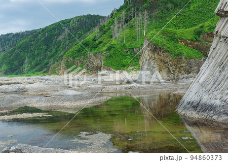 coastal landscape, beautiful columnar basalt cliff on the wooded coast of Kunashir island coastal landscape, beautiful columnar basalt cliff on the wooded coast of Kunashir island 94860373