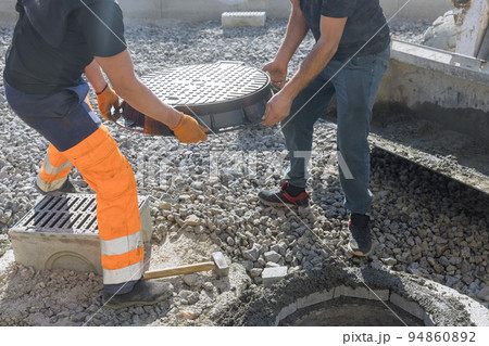 Cast iron sewer hatch being installed on a concrete base as part of the installation of a water sewer well in the ground 94860892