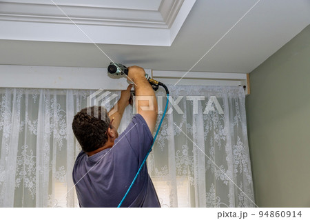 In a newly constructed home, a handyman nails wooden cornices on the curtain wall above a window in a manner that looks professional. In a newly constructed home, a handyman nails wooden cornices on the curtain wall above a window in a manner that looks professional. 94860914