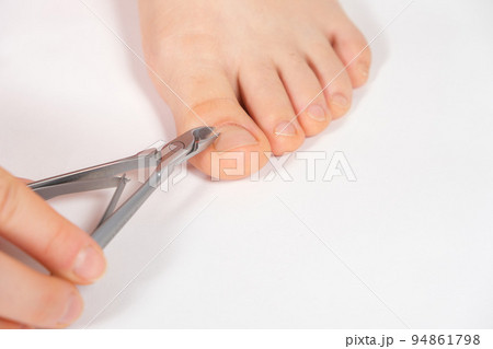 A woman does a pedicure in a beauty salon, removes the cuticle from the big toe with forceps A woman does a pedicure in a beauty salon, removes the cuticle from the big toe with forceps 94861798