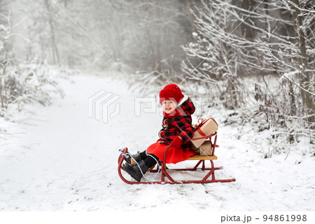 A girl in a plaid coat is sitting in a sled in the woods with a bunch of Christmas gifts tied with a ribbon. It's time to choose and give gifts. The New year is coming soon. copy space A girl in a plaid coat is sitting in a sled in the woods with a bunch of Christmas gifts tied with a ribbon. It's time to choose and give gifts. The New year is coming soon. copy space 94861998