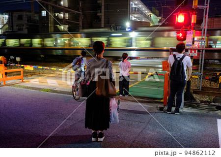 陽が暮れた帰り道。踏切で列車の通過を待つ人々 94862112