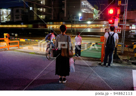 陽が暮れた帰り道。踏切で列車の通過を待つ人々 94862113