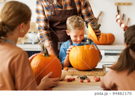 Happy boy smiling while helping dad carve Halloween pumpkin. 94862170