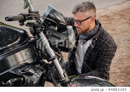 Man biker middle aged motorcyclist smiling sitting with a motorcycle on the side of the road in the forest 94863165