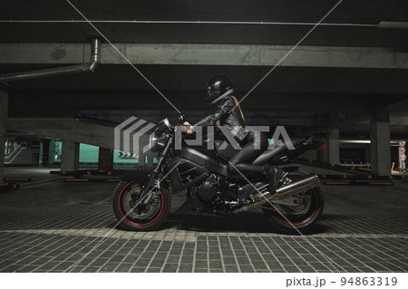 Young woman biker in a helmet sitting on a motorcycle in the underground parking garage Young woman biker in a helmet sitting on a motorcycle in the underground parking garage 94863319